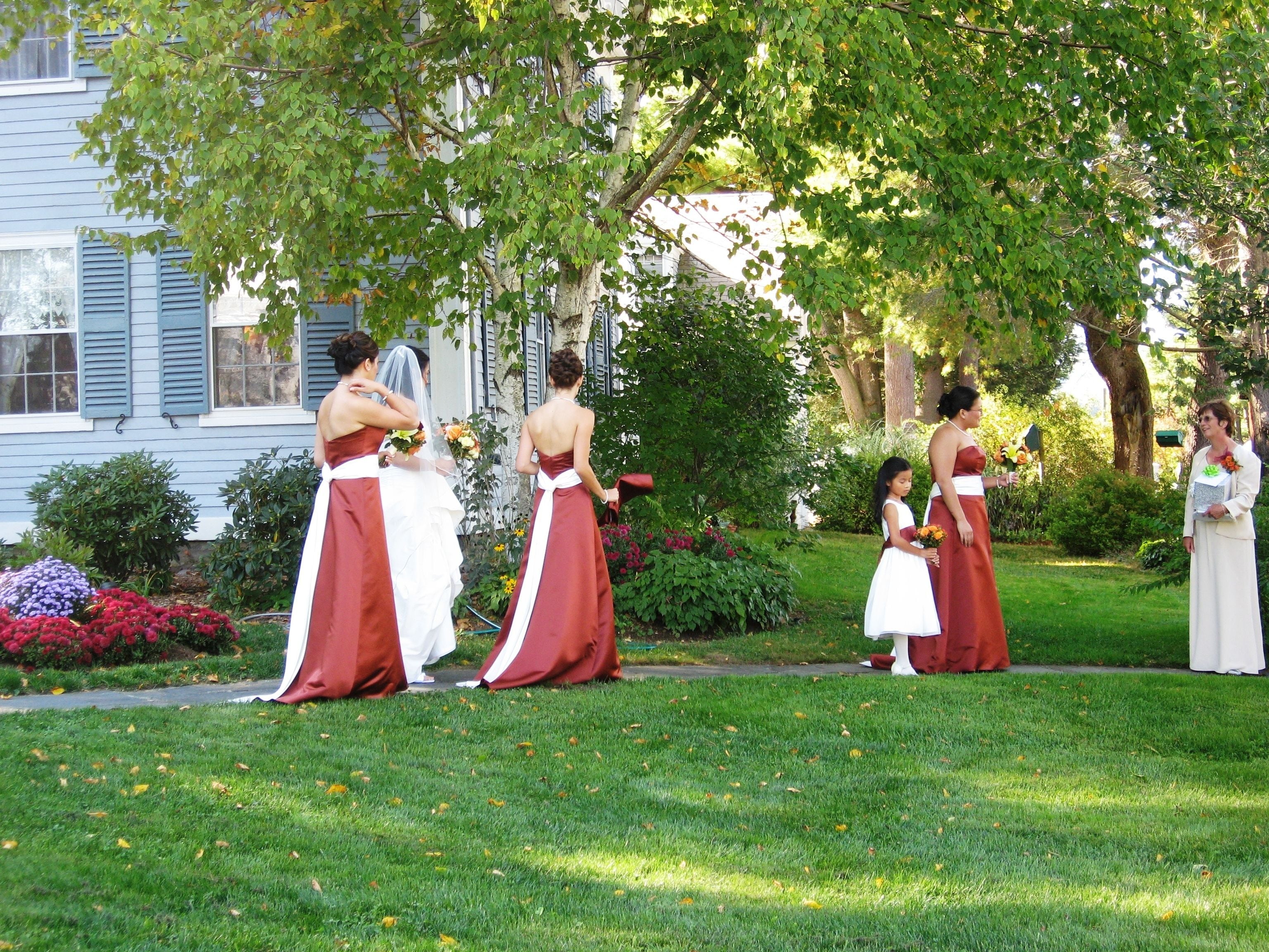 A group of women in formal attire standing in a garden with a house in the background.