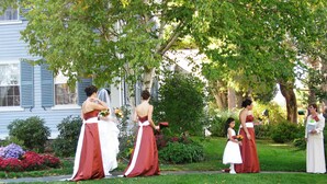 Un grupo de mujeres vestidas formalmente de pie en un jardín con una casa al fondo.