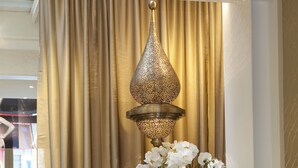 A living room with a purple armchair, a round table with a white orchid, and a gold-colored lamp. - Hotel Mayet (Paris)