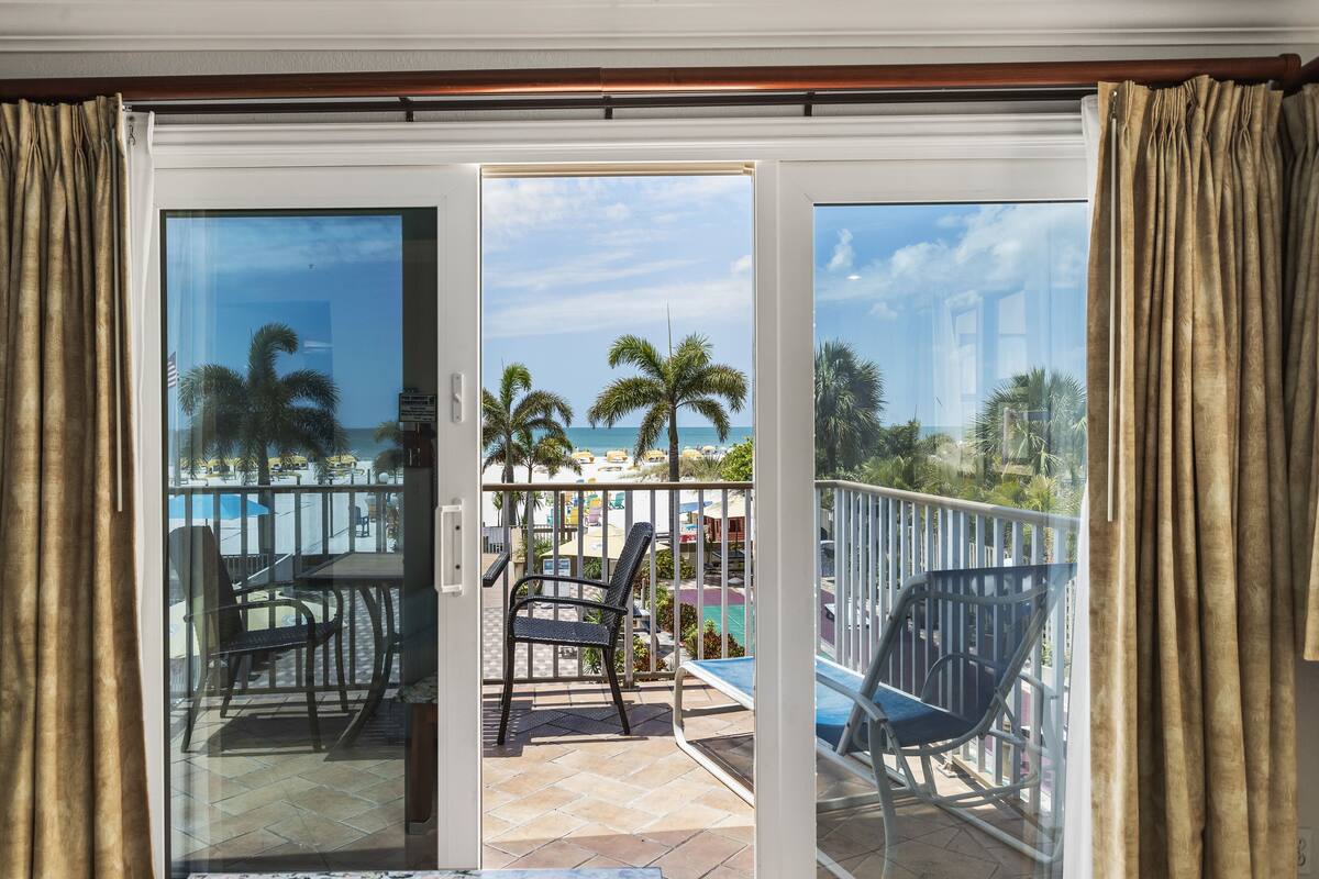 A balcony with a view of the beach, including palm trees and a clear sky.
