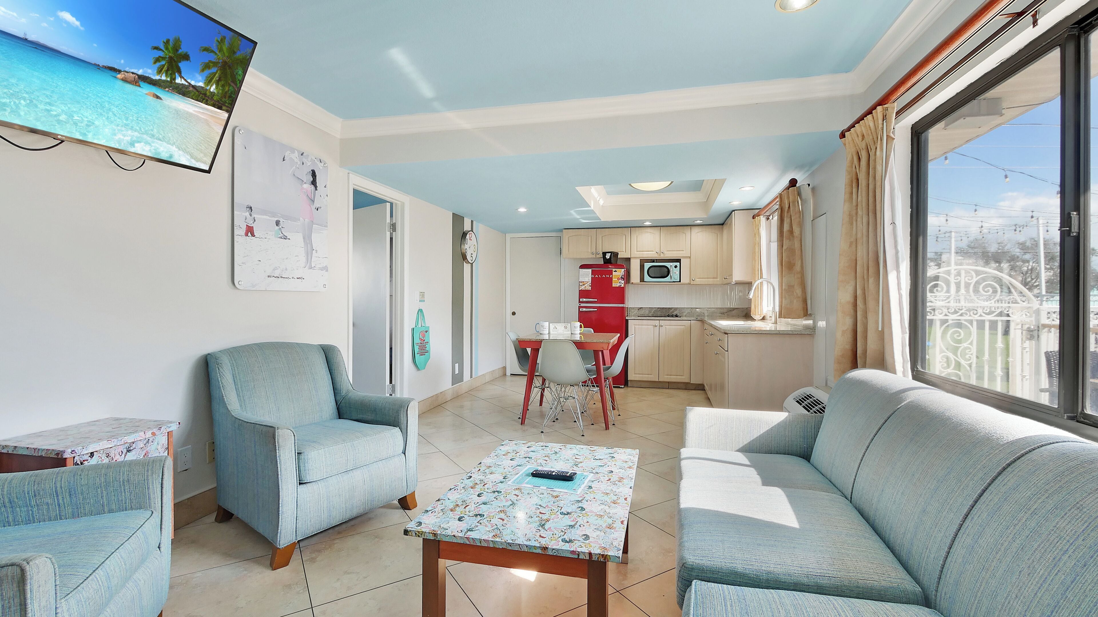 A living room with a sofa, a chair, a table, and a TV displaying a beach scene.