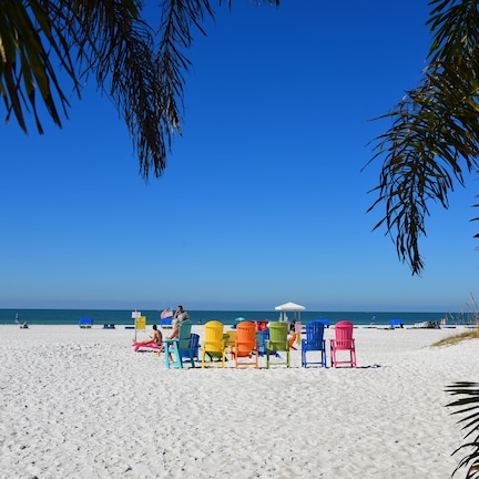 A beach with white sand, clear blue sky, and colorful beach chairs.