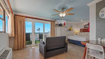 A hotel room with a bed, a desk, a chair, a ceiling fan, and a view of the outdoors.