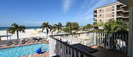 A pool area with a view of the beach, a building with balconies, and palm trees.