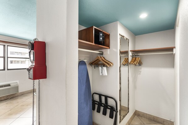 A hotel room with a red telephone, a blue towel, a wooden shelf, and a clothing rack with hangers.