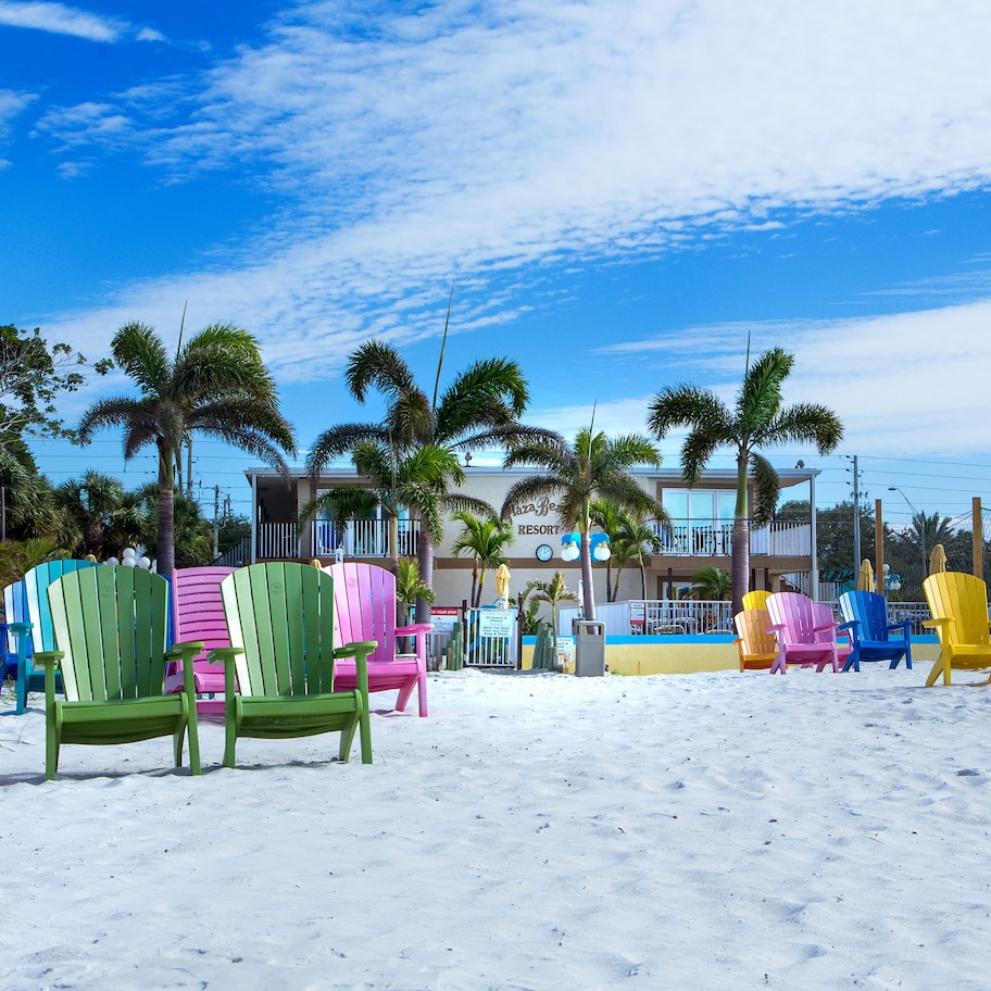 A beach with colorful Adirondack chairs lined up and palm trees in the background.