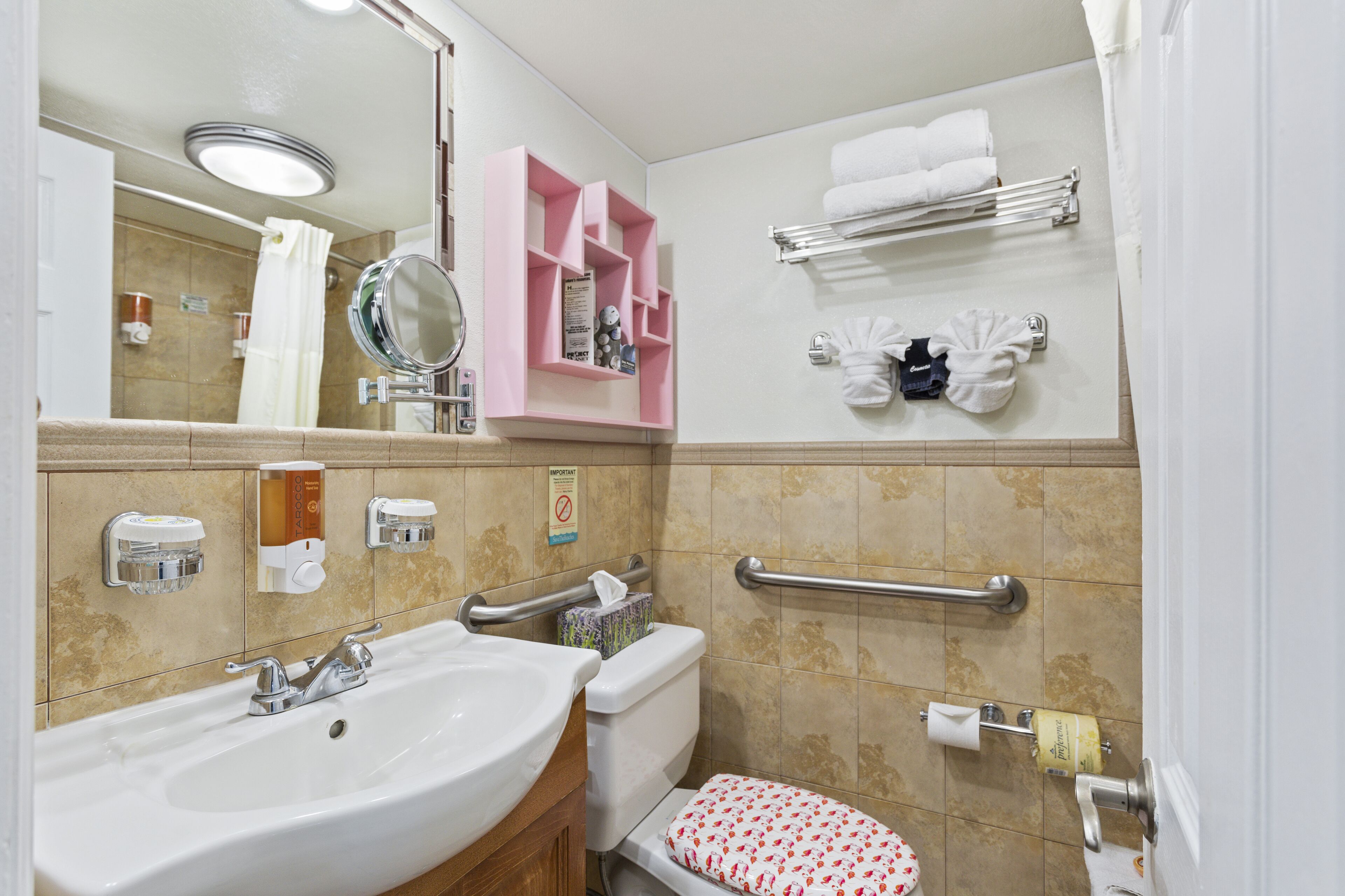 Un baño con lavamanos, espejo, inodoro y ducha. Hay toallas y artículos de aseo en los estantes.