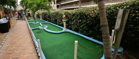 A miniature golf course with a brick pathway, green artificial turf, and palm trees.