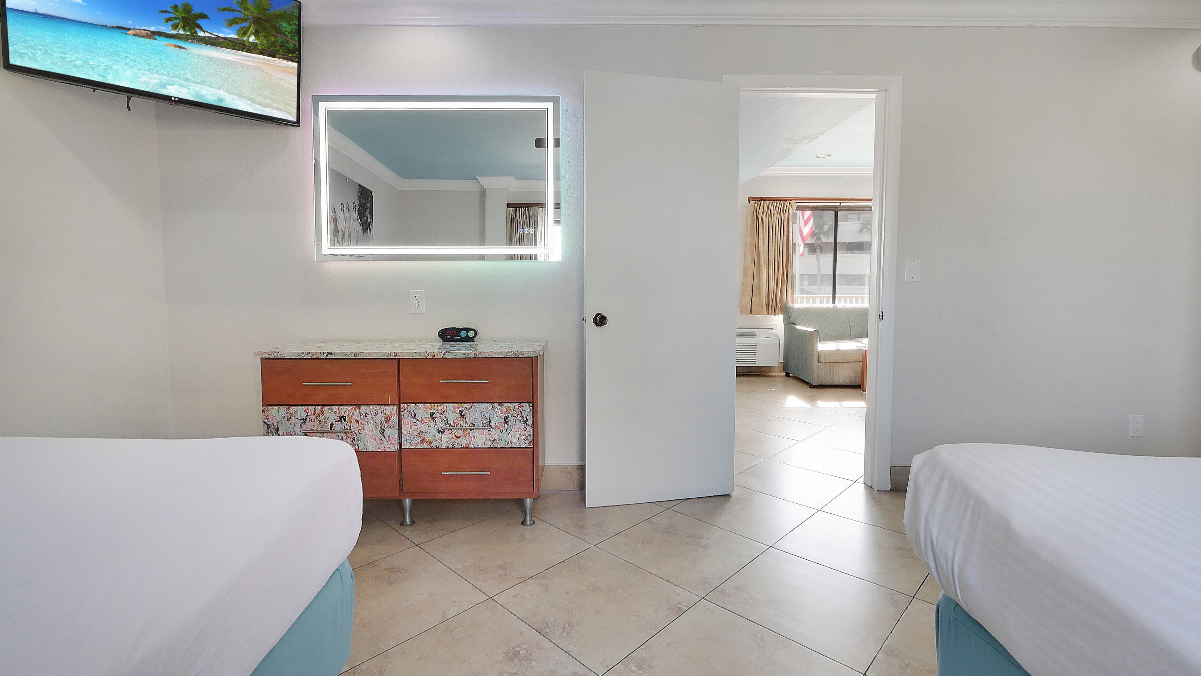 A hotel room with two beds, a vanity with a mirror, a dresser, and a television on the wall.