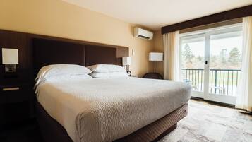 Ein Hotelzimmer mit einem großen Bett, einem Nachttisch mit Lampe, einer Klimaanlage und Blick ins Freie durch eine Schiebetür.