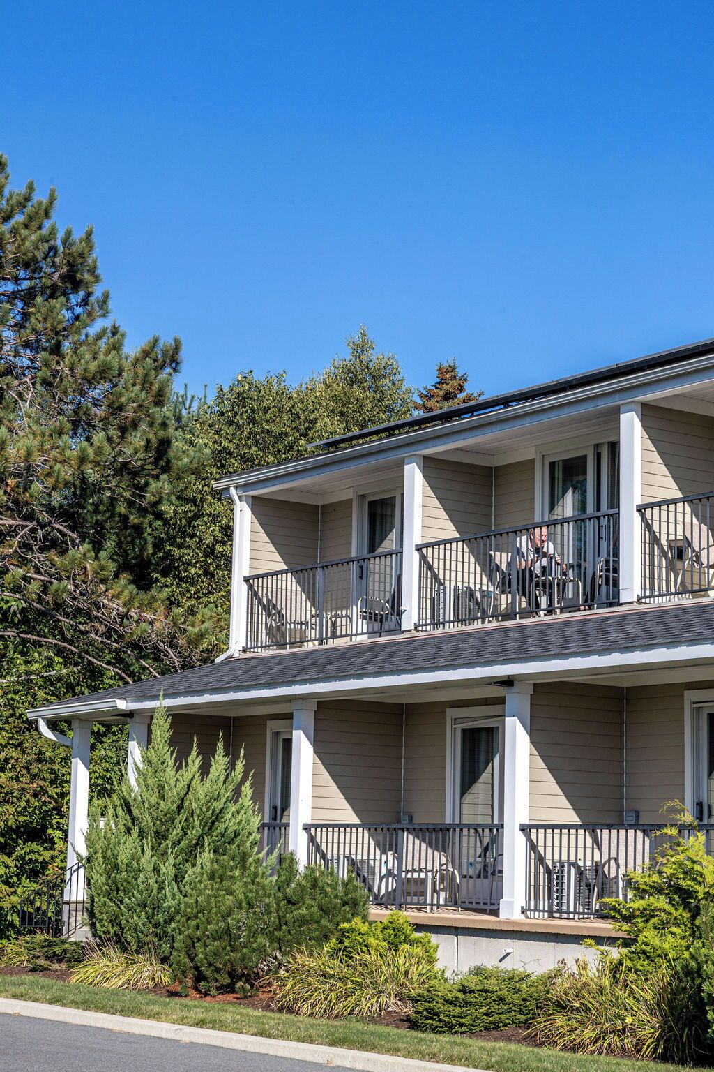 A two-story building with a balcony on the upper floor, a covered front porch, and a landscaped front yard.