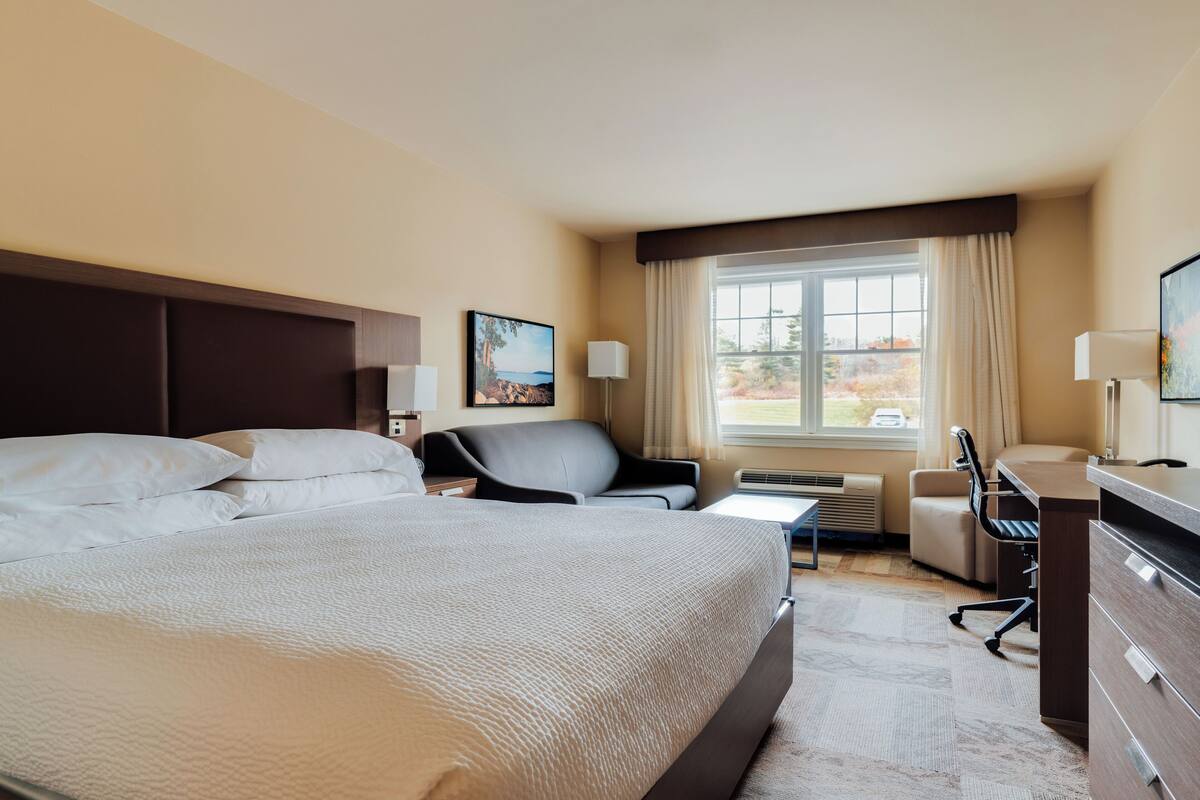 Ein Hotelzimmer mit einem großen Bett, zwei Sesseln, einem Schreibtisch und einem Fenster mit Blick ins Freie.