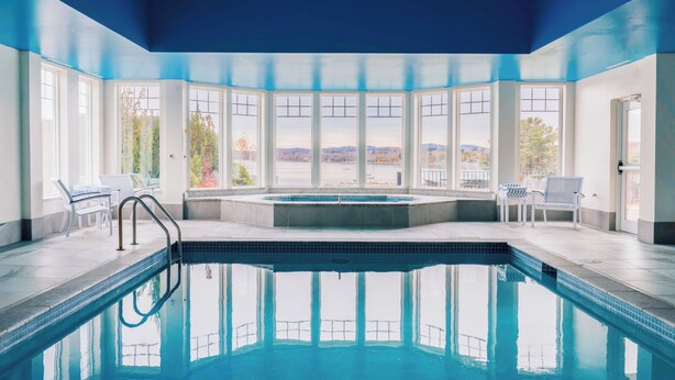 A swimming pool with a view of a lake and hills, surrounded by white walls and large windows. - Belfast Harbor Inn (Belfast)