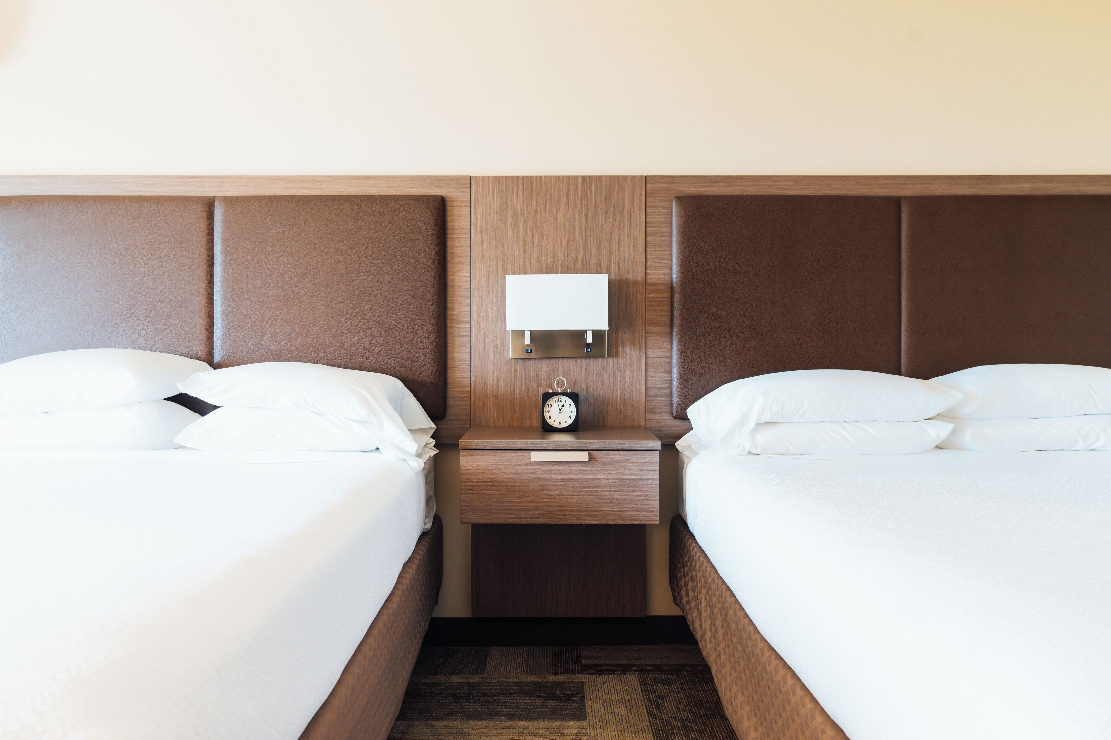 Ein Hotelzimmer mit zwei Betten, einem Nachttisch mit einer Uhr und einer Wandleuchte.