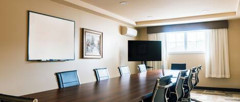 A conference room with a long table, six chairs, a flat-screen TV, a whiteboard, and a window with curtains.