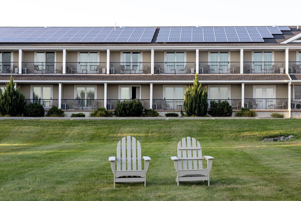 Un motel con una fila de habitaciones, césped y dos sillas Adirondack.