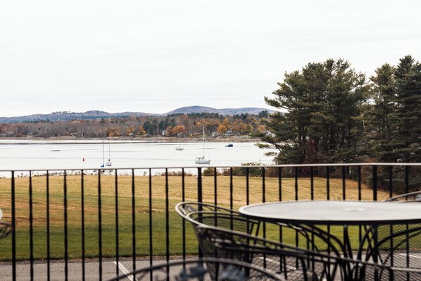 A balcony with a table and chairs overlooking a body of water with boats, surrounded by trees and hills. - Belfast Harbor Inn (Belfast)