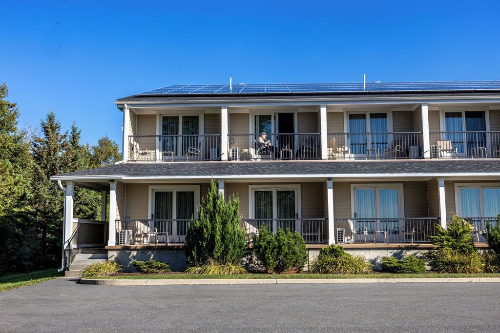 Un edificio de dos pisos con un balcón en el nivel superior, un porche cubierto en la parte delantera y paneles solares en el techo.