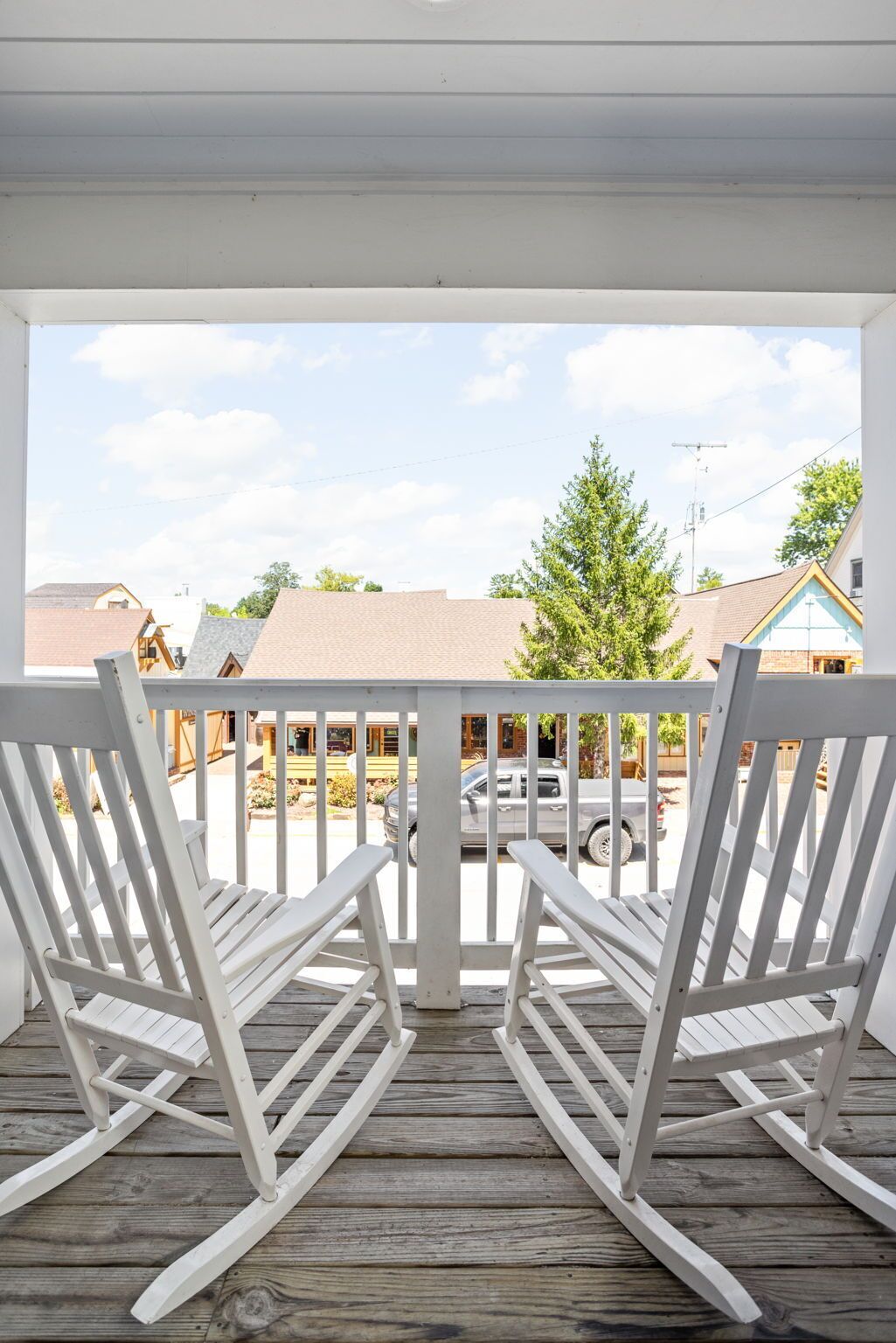 Um deck de madeira com cadeiras de balanço brancas e vista para uma rua residencial.