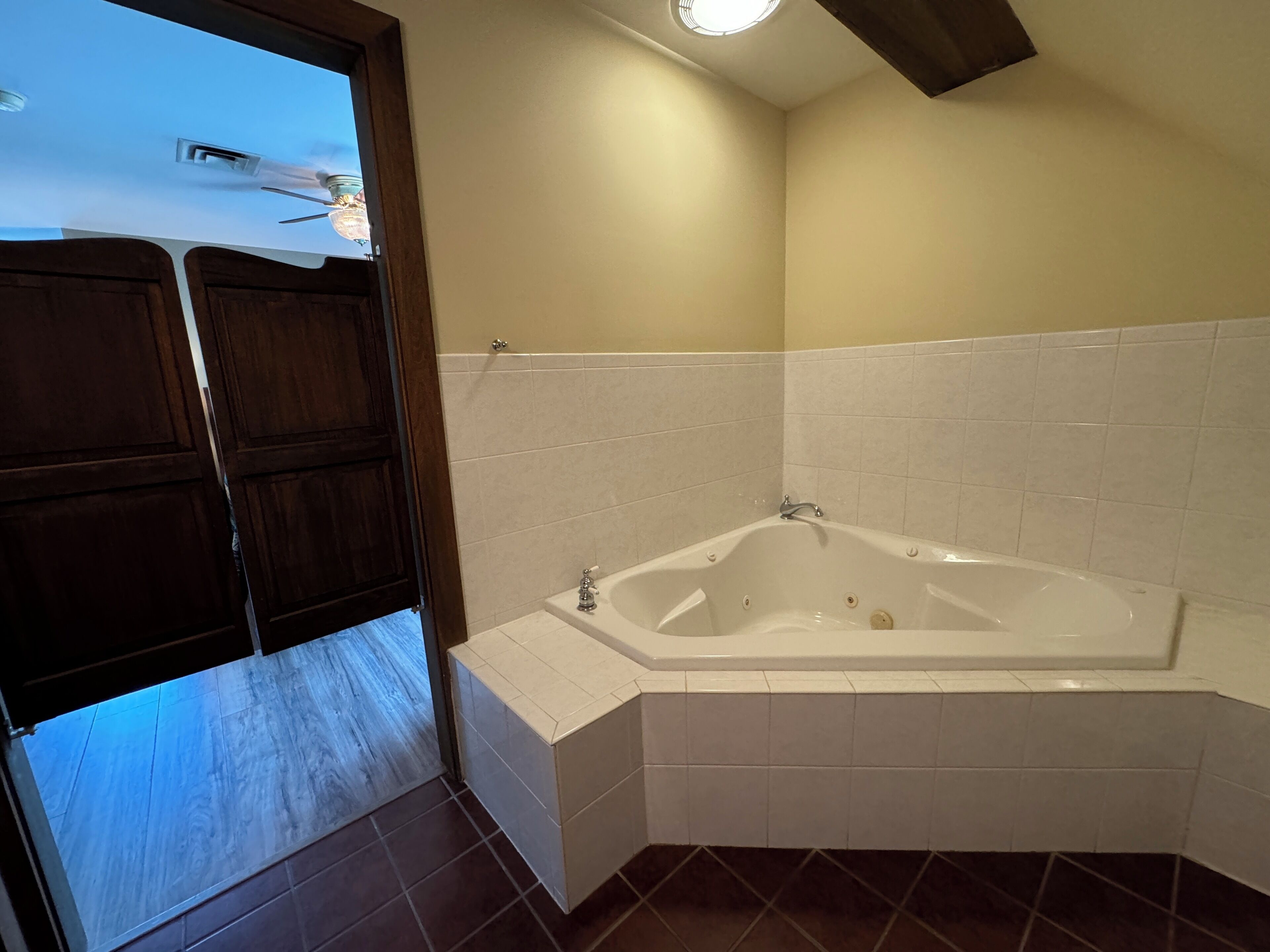 A bathroom with a corner bathtub, white tiled walls, and a wooden door.