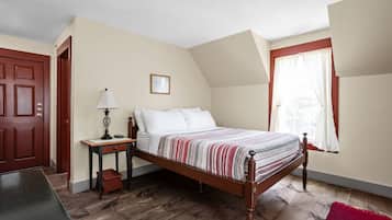 A bedroom with a wooden bed, a nightstand, a desk, a chair, a red rug, a door, and a window with curtains.
