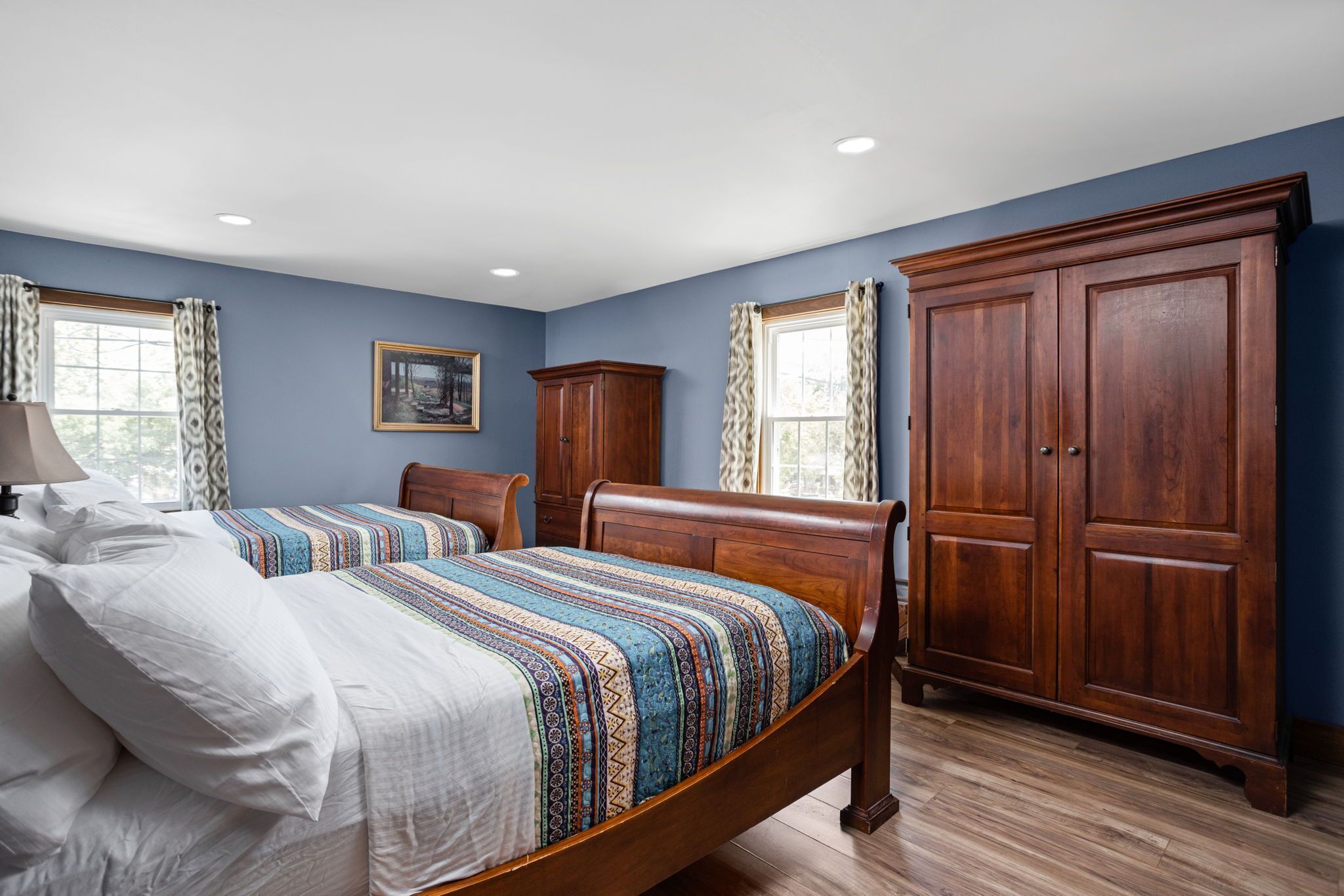 Quarto com cama de madeira, duas mesas de cabeceira, guarda-roupa e janela com cortinas.