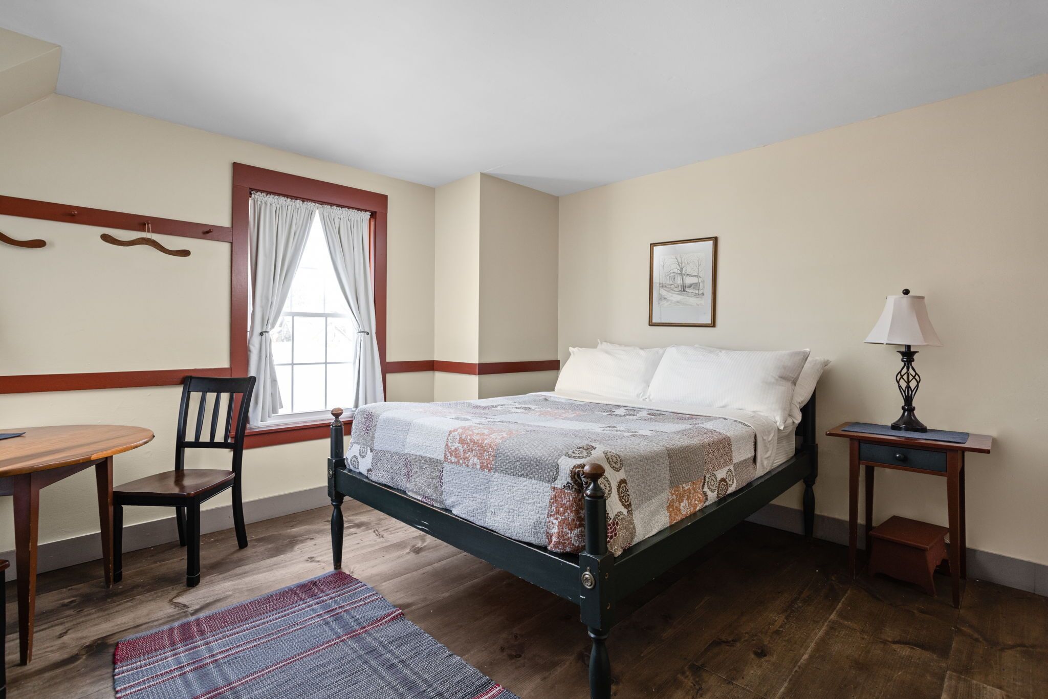 A bedroom with a bed, a chair, a table, a lamp, and a window with curtains.