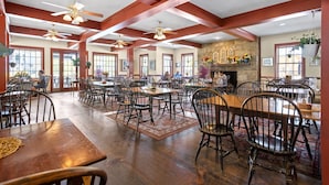 Un vaste espace dédié à la salle à manger, avec des tables et des chaises en bois, une cheminée en pierre et de grandes fenêtres.