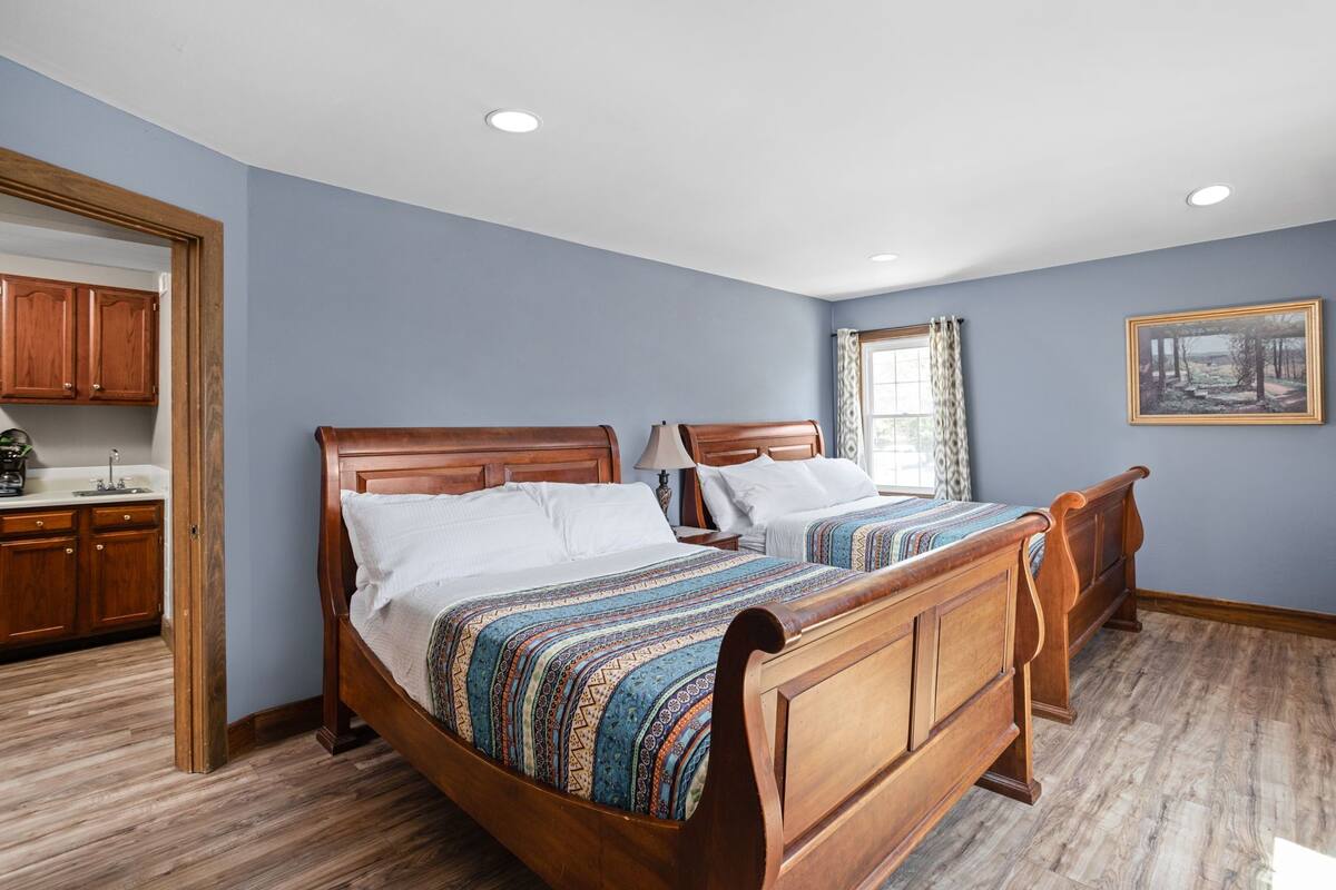 A bedroom with two wooden beds, a window with curtains, and a painting on the wall.