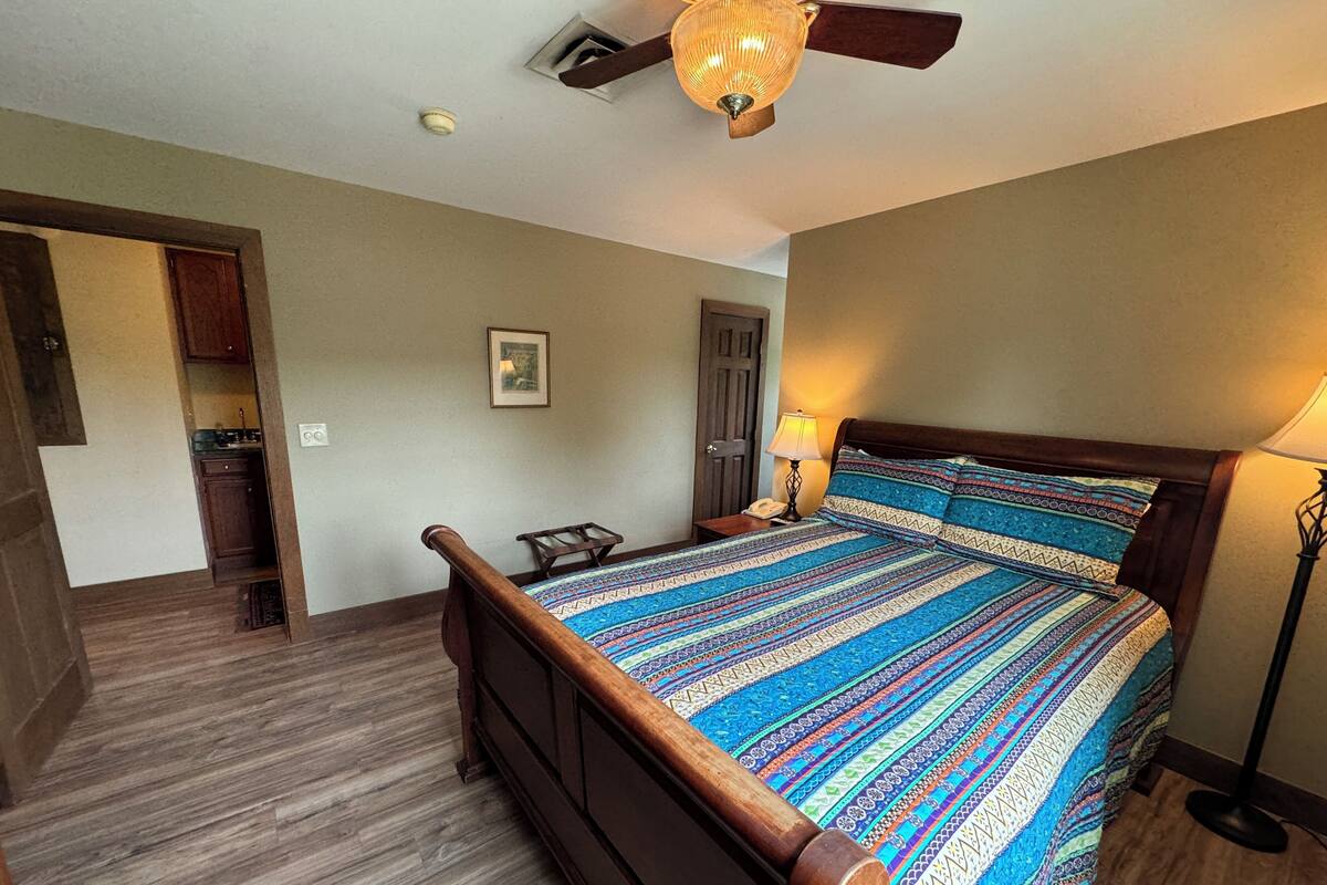 A bedroom with a wooden bed, a nightstand, a lamp, and a ceiling fan.