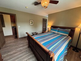 A bedroom with a wooden bed, a nightstand, a lamp, and a ceiling fan.