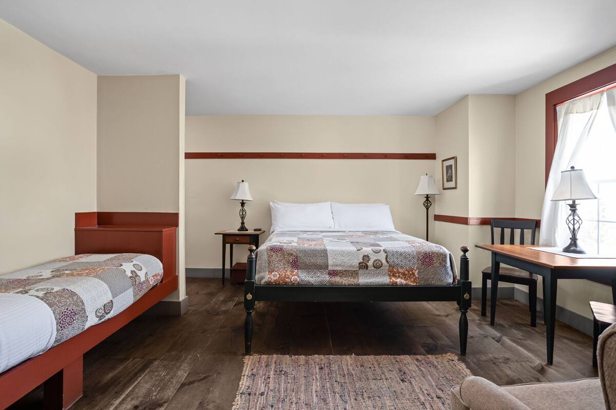 A bedroom with a large bed, two smaller beds, a desk, and a chair.