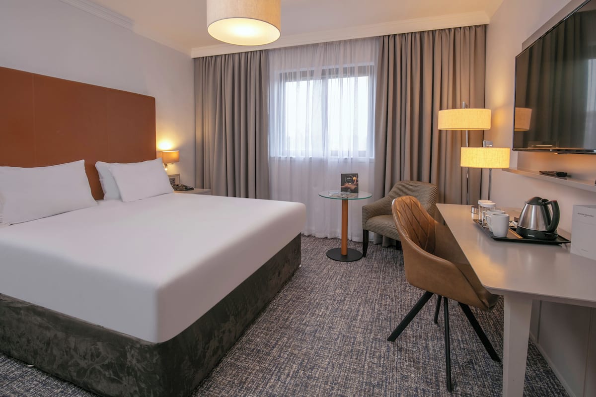 Een hotelkamer met een groot bed, een bureau met stoel, een koffiezetapparaat en een televisie.