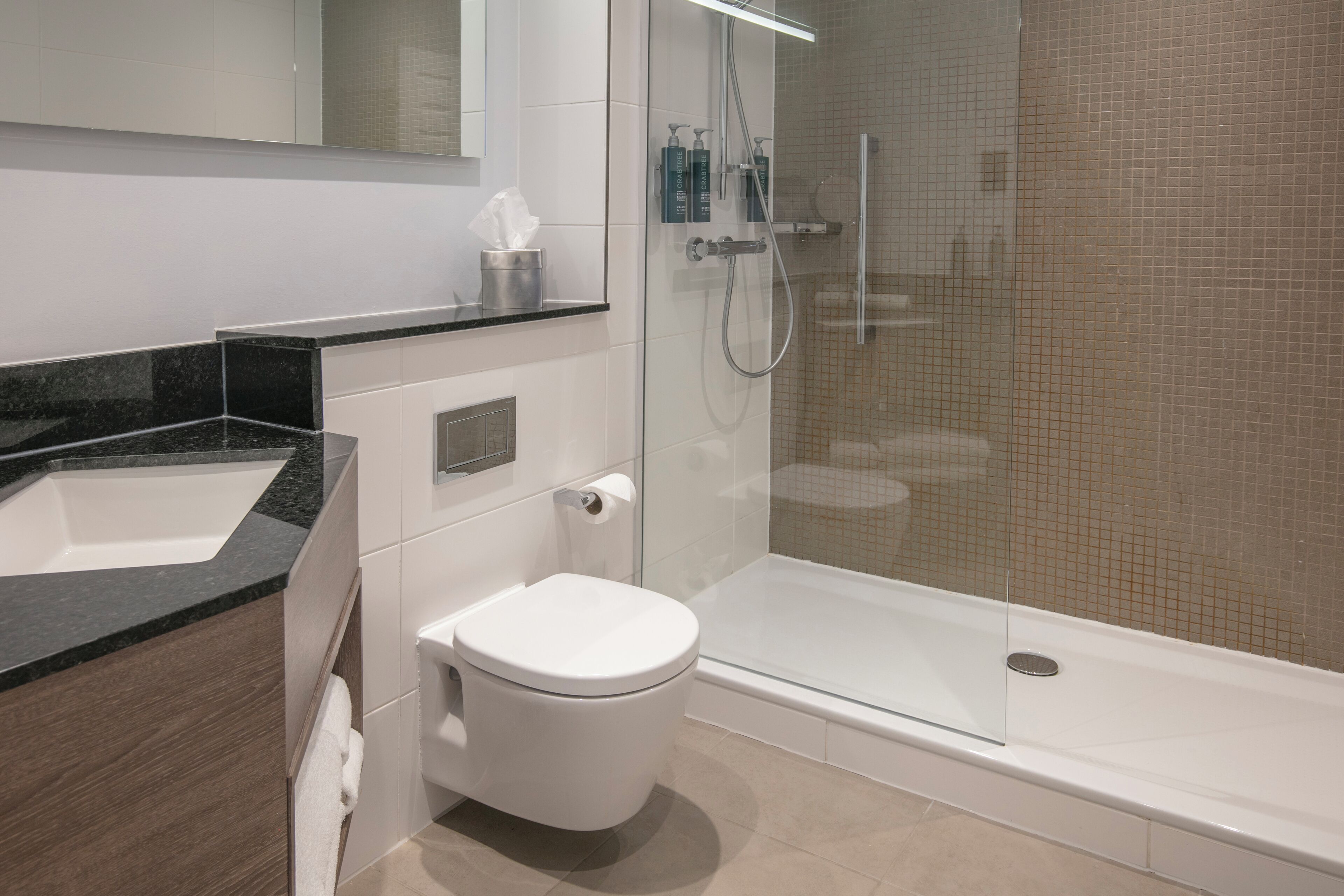 A modern bathroom with a white toilet, a glass-enclosed shower, a black countertop, and a white sink.
