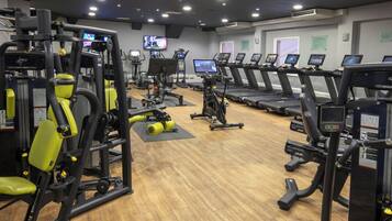 A gym with various exercise machines, treadmills, and a television screen displaying workout videos.