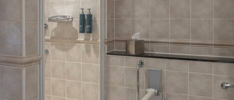 A bathroom with a glass-enclosed shower, a toilet, and a shelf with toiletries.