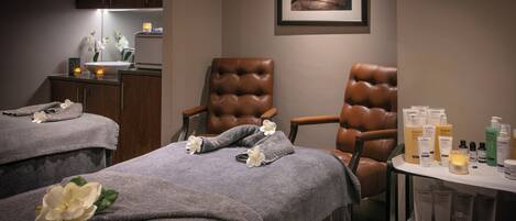 A spa room with two massage tables, a brown leather chair, and a shelf with skincare products.