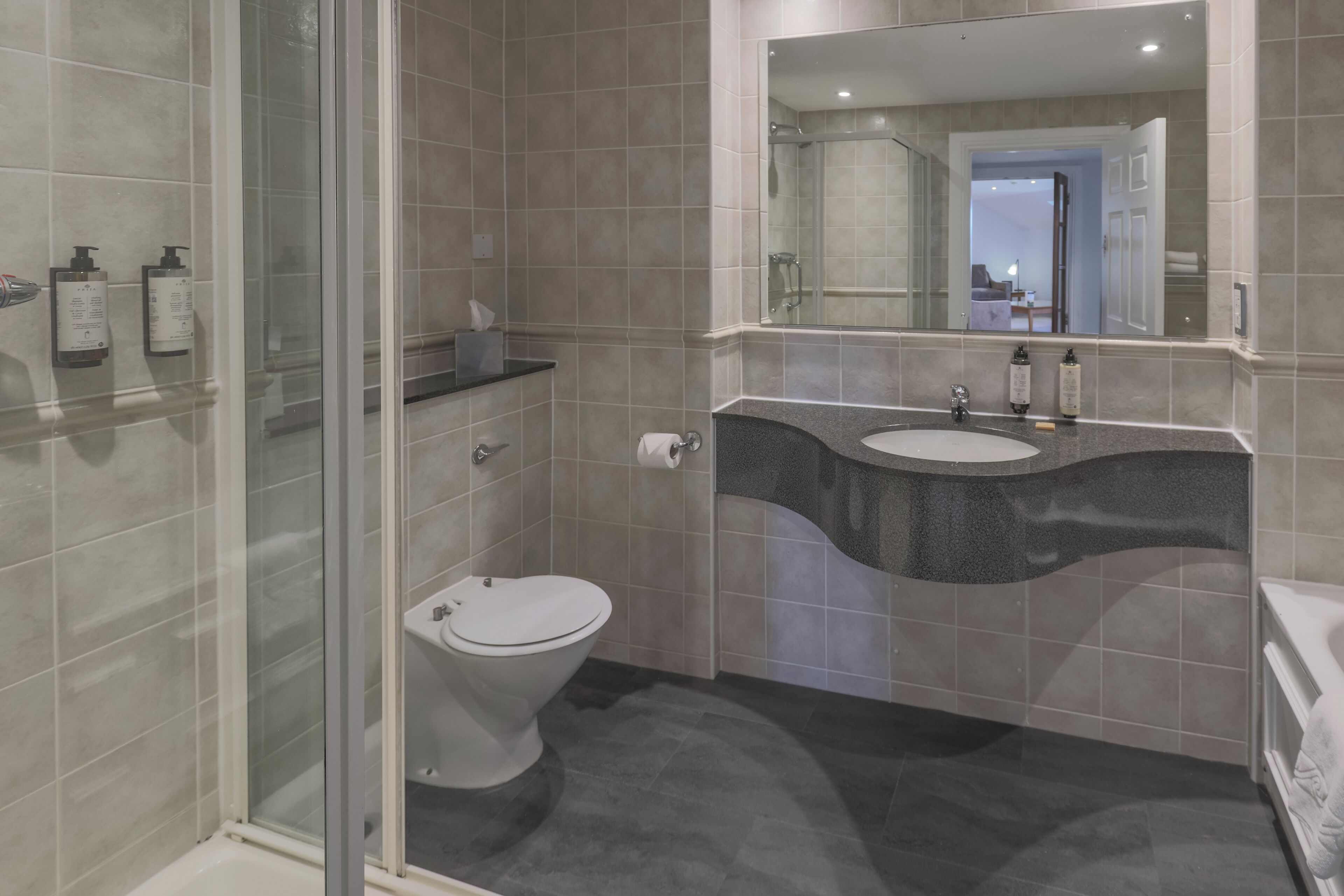 A modern bathroom with a glass shower enclosure, a toilet, a sink with a curved countertop, and a large mirror above the sink.