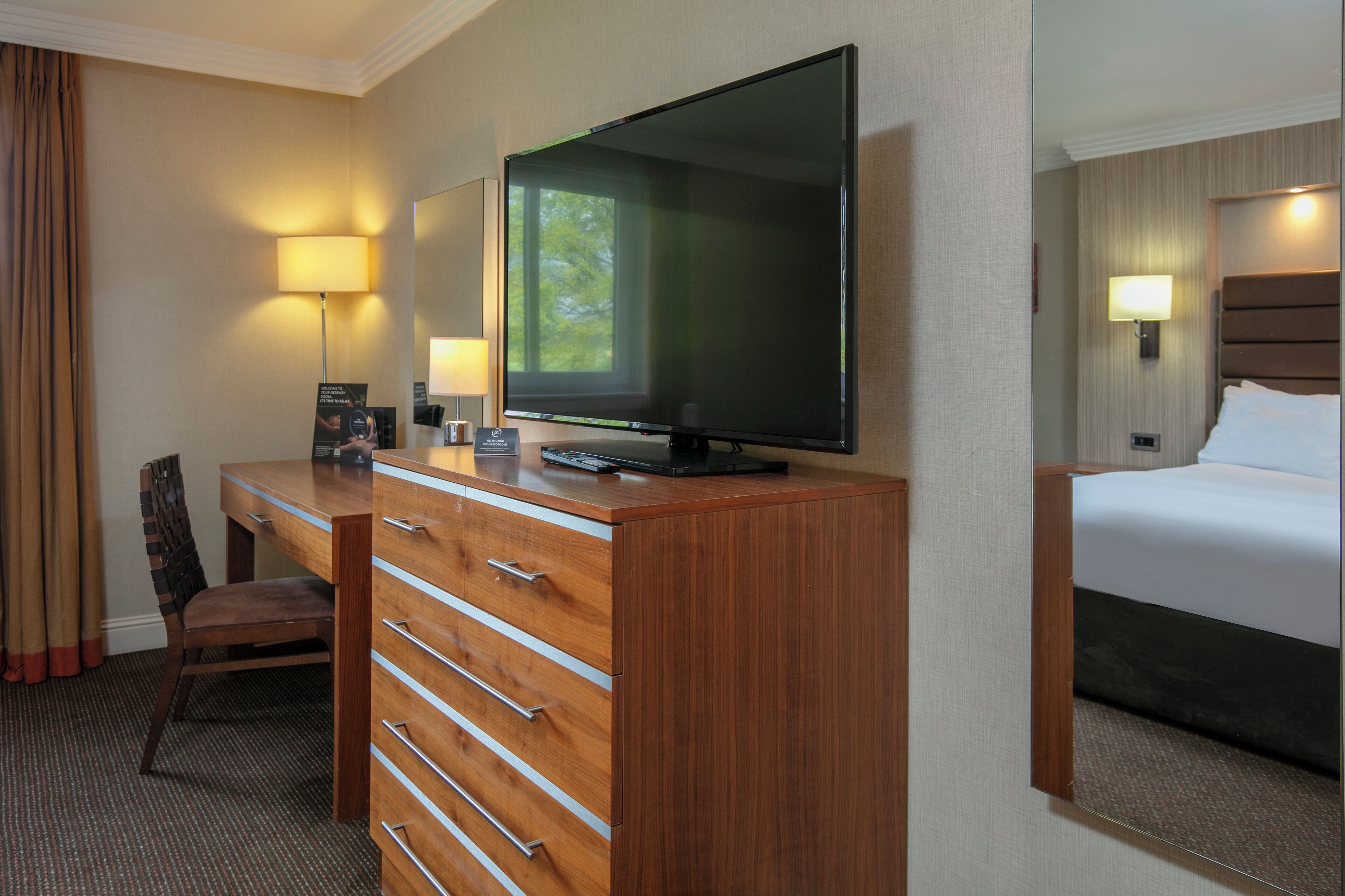 Una habitación de hotel con un escritorio de madera, un televisor de pantalla plana, una cama y una silla.