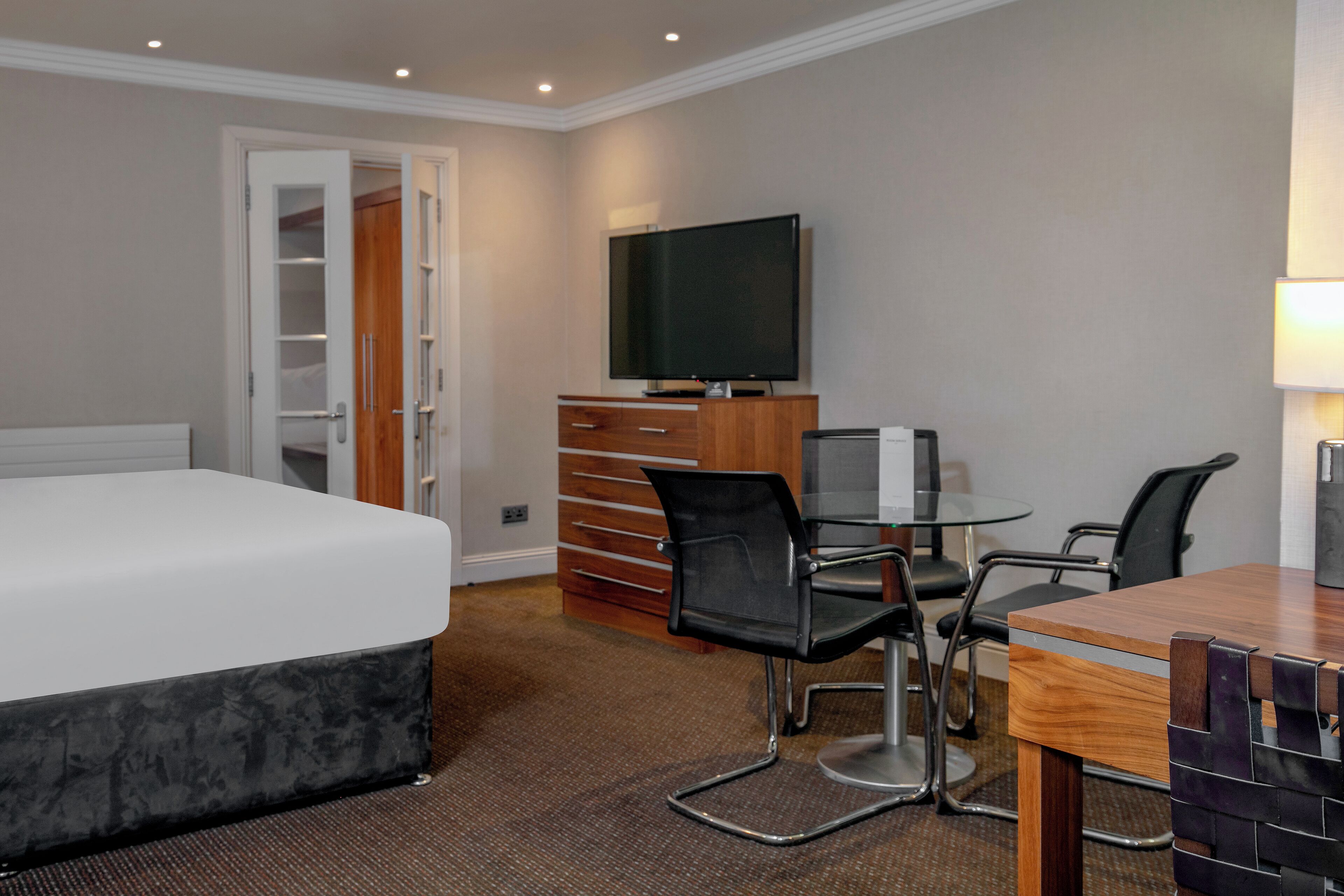 Ein Hotelzimmer mit einem Bett, einem Schreibtisch mit Stühlen, einem Fernseher und einem Kleiderschrank.