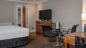 A hotel room with a bed, a desk with chairs, a television, and a wardrobe.
