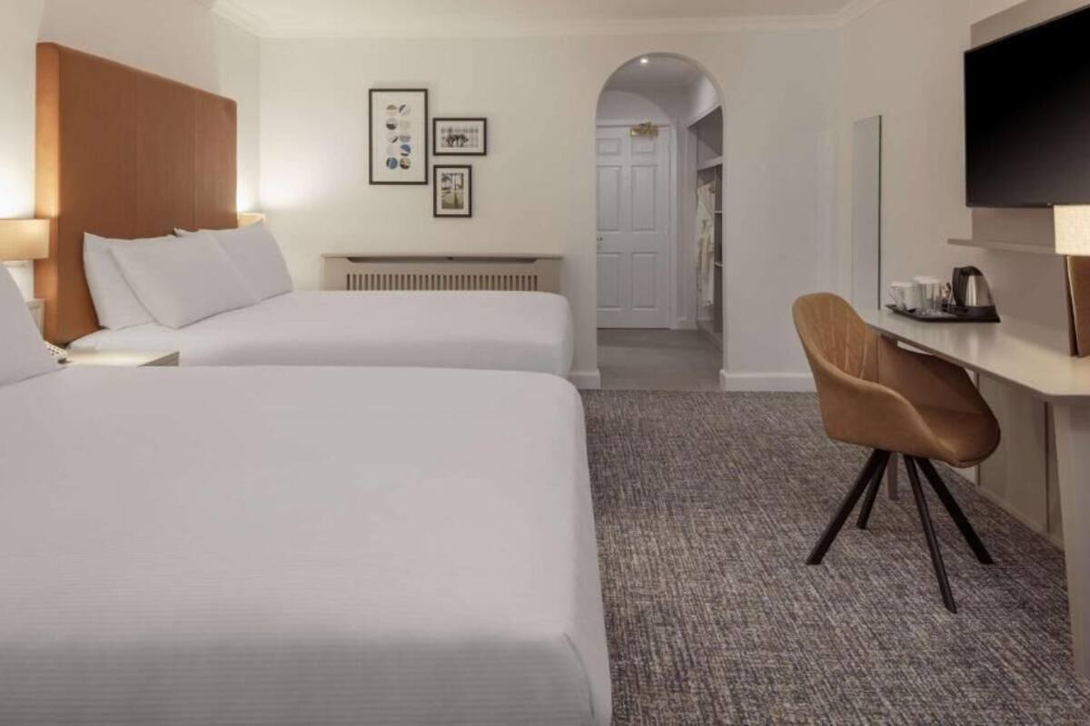 Een hotelkamer met twee bedden, een bureau met stoel, een televisie en fotolijstjes aan de muur.