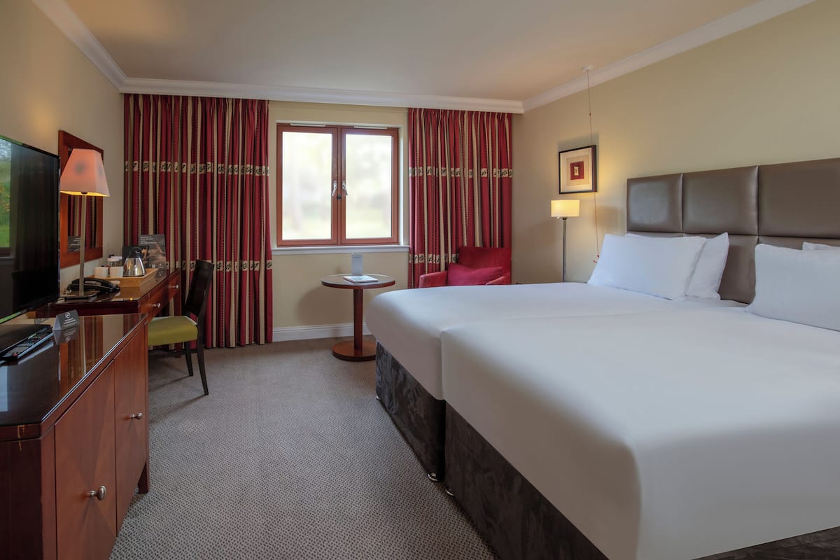 Een hotelkamer met een groot bed, een bureau met een televisie, een stoel, een klein tafeltje en gordijnen.