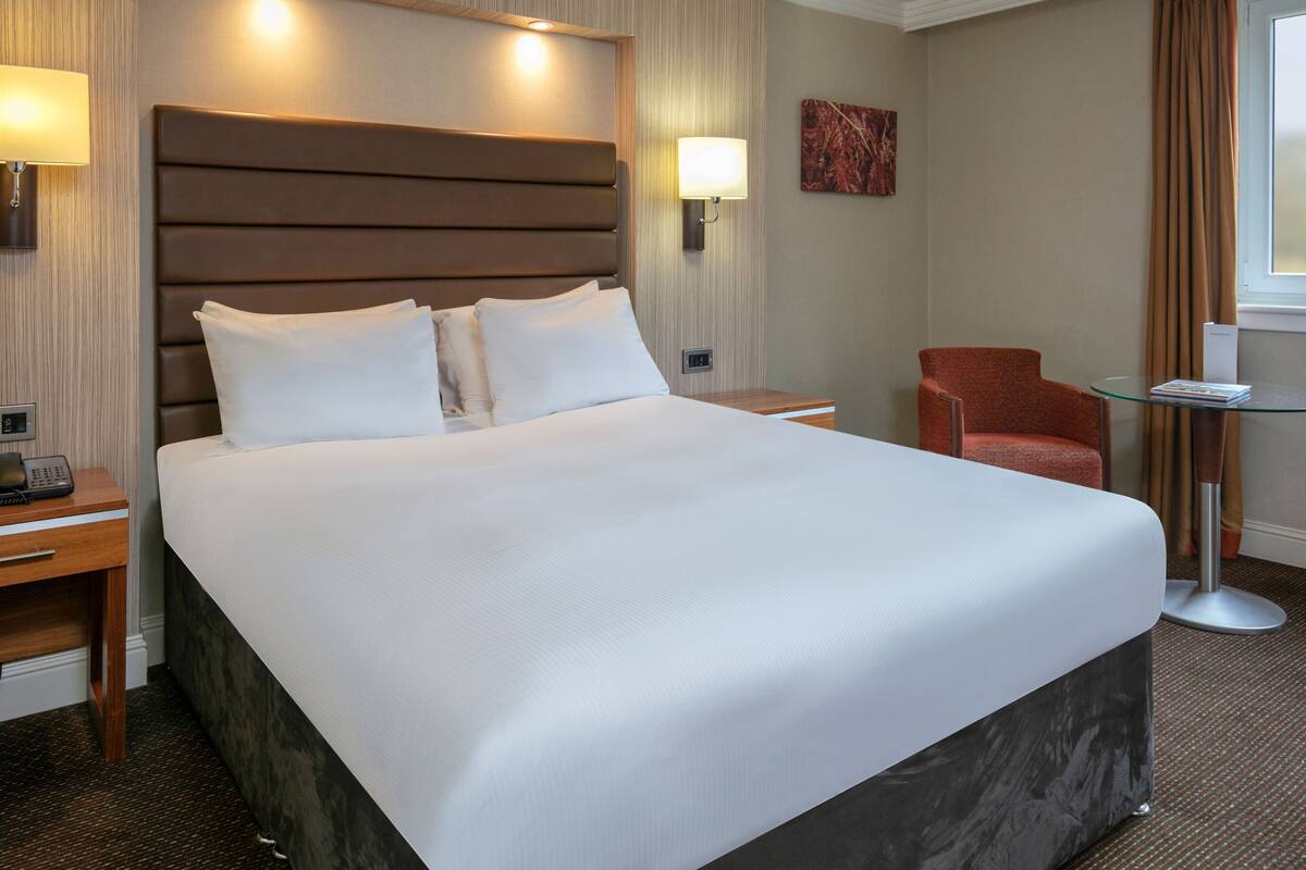 Een hotelkamer met een groot bed, nachtkastjes, een stoel, een tafeltje en een lamp.