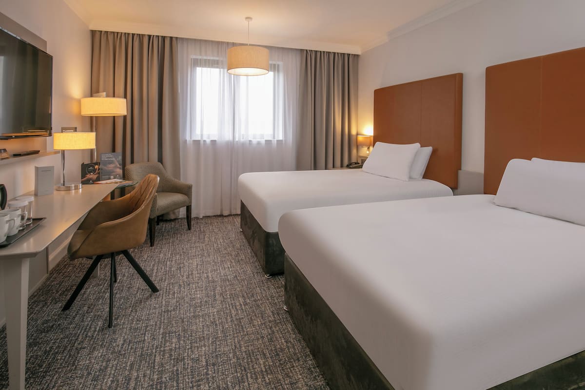 Hotelkamer met twee bedden, een bureau, een stoel, een televisie en een raam met gordijnen.