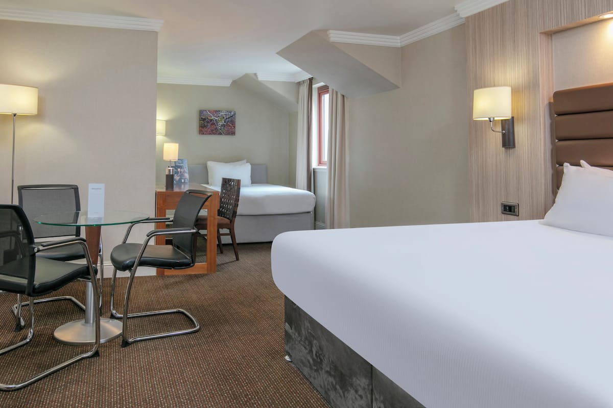 Een hotelkamer met een groot bed, een bureau met twee stoelen, een lamp en een schilderij aan de muur.