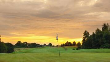A golf course with a flagstick in the foreground and a sunset in the background.