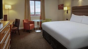 Habitación de hotel con una cama grande, un escritorio, una silla, una mesita y un televisor.