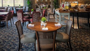 Een restaurantgedeelte in een hotel met een grote ronde tafel, meerdere stoelen, een kroonluchter en een buffet.