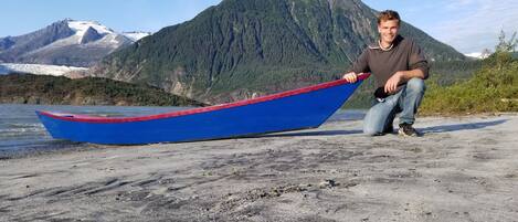 A man holding a blue boat on a concrete surface with a mountainous background.